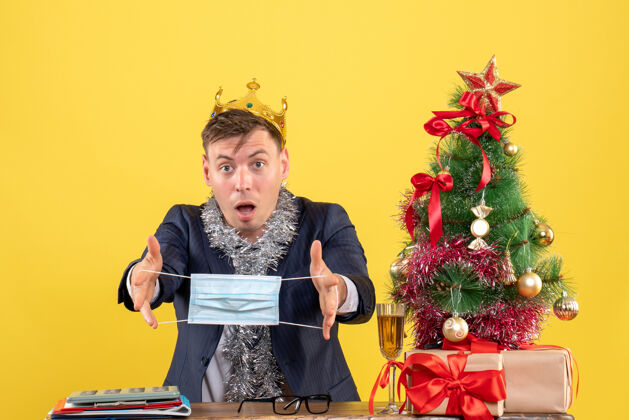 生意商务人士戴着皇冠面具坐在圣诞树旁的桌子前 黄色的礼物桌子人黄色