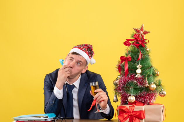 桌子商务人士使用noisemaker坐在圣诞树旁的桌子前 呈现黄色使用礼物男性