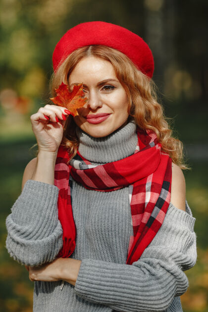开朗漂亮女人的样子穿着红色贝雷帽的时髦女孩手里拿着树叶的女士女人黄色金发