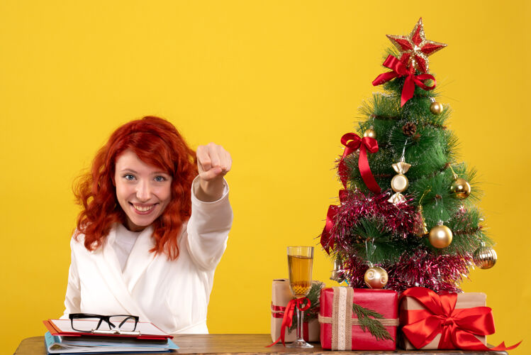 女工人女工人坐在桌子后面 拿着圣诞树和黄色的礼物礼物女办公室