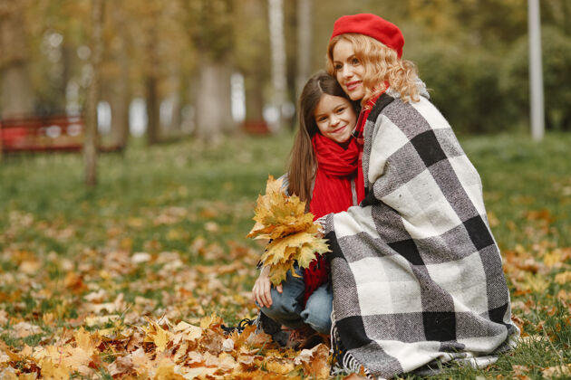 毛毯时髦的母亲带着女儿黄色的秋天戴着红领巾的女人一起家庭叶子