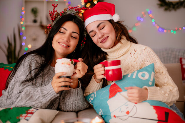 快乐可爱的年轻女孩戴着圣诞帽 拿着杯子坐在扶手椅上 在家里享受圣诞时光举行女孩杯子