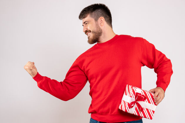 举行身穿红衫的年轻人手持圣诞礼物站在白墙上的正视图微笑圣诞节成人