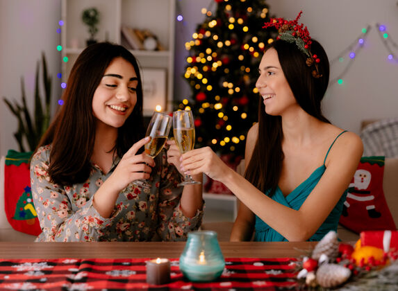 香槟可爱的年轻姑娘们坐在桌旁 碰杯香槟 在家里享受圣诞时光杯子享受快乐