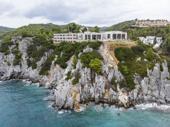 北希腊爱琴海沿岸 卢特拉建筑位于岩石峭壁附近 绿意盎然 海水湛蓝从无人驾驶飞机上俯瞰海岸线海洋场景