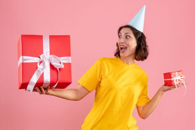 年轻一个年轻女子手持圣诞礼物在粉红色墙上的前视图成人购物者可爱