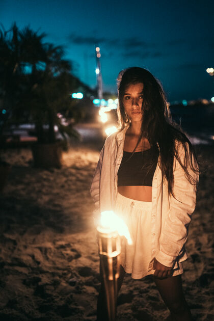 浪漫一个穿着白衣服拿着手电筒的年轻女人晚上在海滩上模型黄昏热