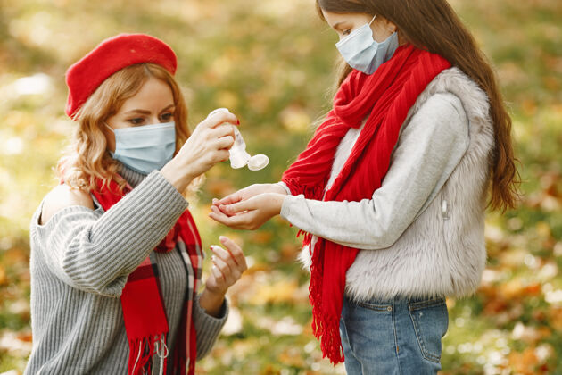 小秋天公园里的一家人冠状病毒主题母亲带女儿人们用杀菌剂贝雷帽秋天户外
