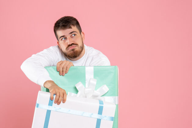 年轻浅粉色墙上礼物盒内年轻人的正面图圣诞节灯光男性