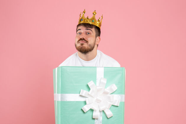帽子年轻人在礼物盒内的正面视图 粉红色墙上有皇冠男人聚会年轻男性