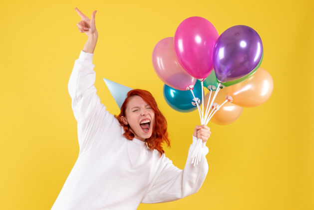 女性黄色墙壁上手持彩色气球的年轻女子的正视图聚会气球生日