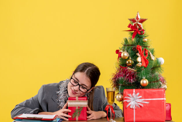 树前视图闭着眼睛的年轻女孩戴着眼镜坐在桌子旁 手里拿着圣诞树和鸡尾酒鸡尾酒年轻女孩抱着