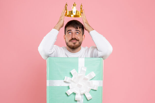 人粉红色墙上戴着王冠的礼物盒内年轻人的正面图快乐前面男性