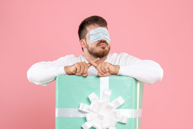 圣诞节粉红色墙上戴着面具的年轻人在礼物盒里的正视图粉色前面情感