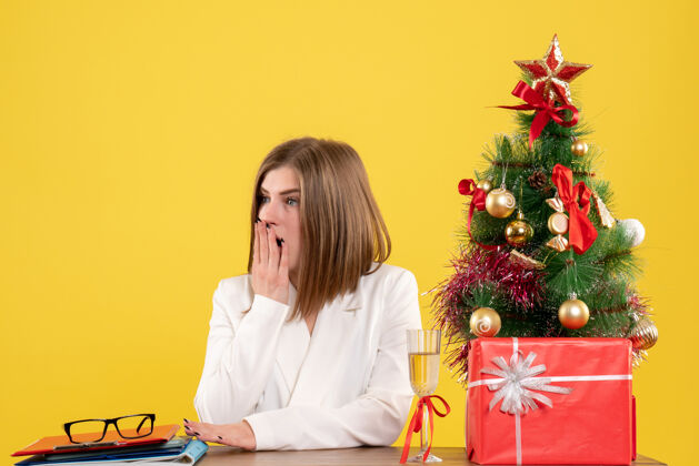 人正面图：女医生坐在黄色背景的桌子前 放着圣诞树和礼品盒电脑坐女