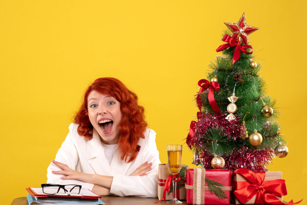 花女工人坐在桌子后面 手里拿着圣诞礼物和黄色的圣诞树情感坐着桌子