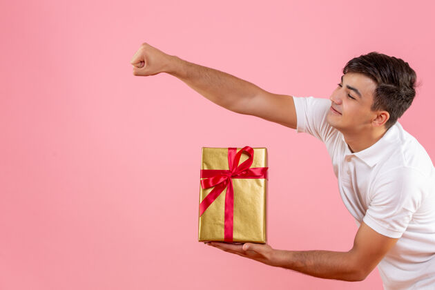 人在粉红色的墙上年轻人给某人送圣诞礼物的正面图庆祝十二月男性