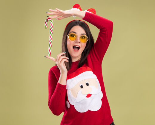 新的令人印象深刻的年轻漂亮的白人女孩穿着圣诞老人毛衣和头带眼镜举行传统的圣诞糖果手杖垂直垂直头带眼镜