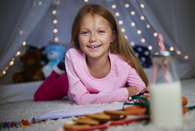 圣诞节开朗的女孩一边画画一边摆姿势牙牙学语的微笑晚上节日