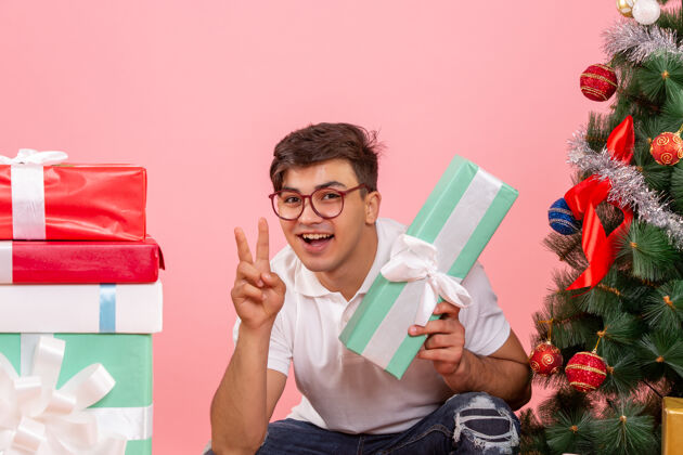 节日年轻人围着礼物和粉红色墙上的圣诞树的正视图礼品盒圣诞快乐庆祝