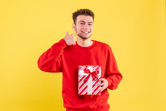 肖像正面图身着红色衬衫的年轻男子微笑着送上圣诞礼物年轻男性红色礼物
