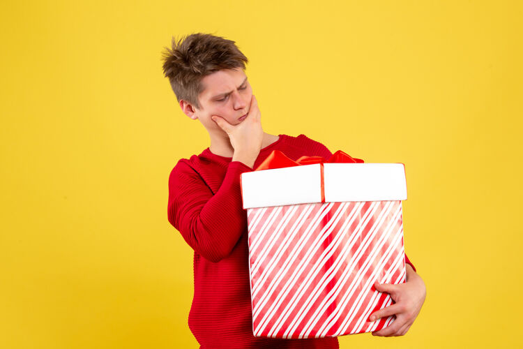 礼盒年轻人拿着大圣诞礼物在黄色墙上思考的正面图情感圣诞快乐人