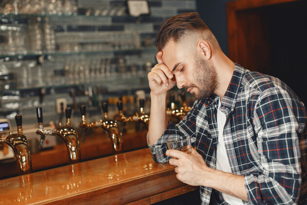 休息一个穿衬衫的男人手里拿着一个玻璃杯那个家伙正坐在酒吧里 抱着他的头白兰地餐厅领带