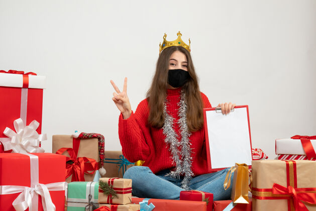 礼物穿着红色毛衣拿着文件做v手势的年轻女孩围坐在礼物旁边 白色的面具上戴着黑色的面具面具年轻女孩文件