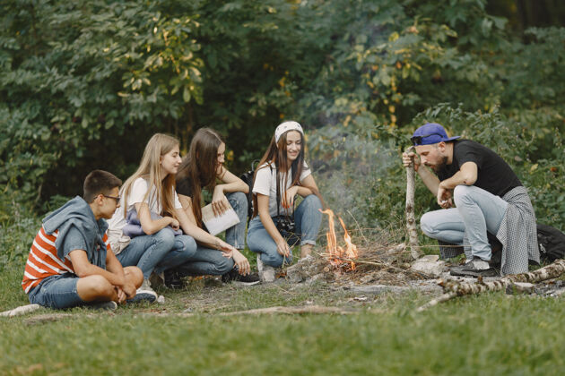 朋友探险 旅游 远足和人的概念一群微笑的朋友在森林里人们坐在篝火旁活跃户外乡村