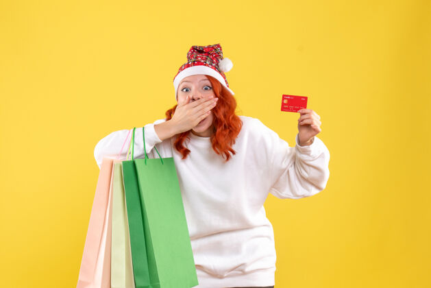 年轻女性黄墙上拿着购物包和银行卡的年轻女子的正视图持有圣诞节情感