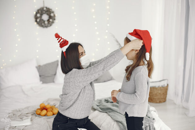 黑发为圣诞节做准备的人冠状病毒主题妈妈和女儿玩穿着灰色毛衣的孩子装饰病毒传统