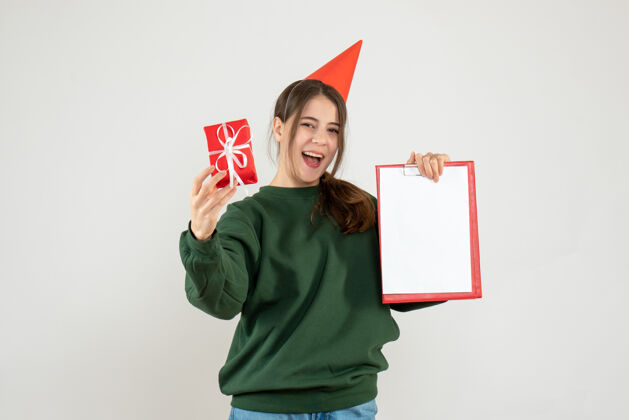 女孩戴着派对帽的快乐女孩指着她的圣诞礼物和白色的文件帽子圣诞节礼物