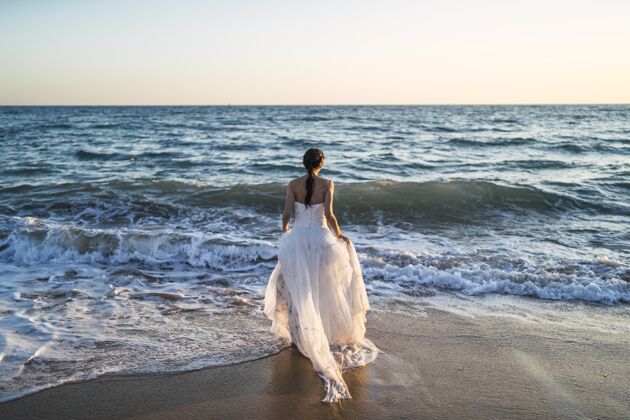 新娘黑发白人新娘穿着白色婚纱走向大海女性黑发自然
