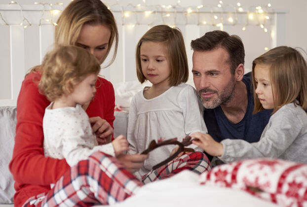 室内父母和孩子在床上度过圣诞节的早晨放松债券装饰