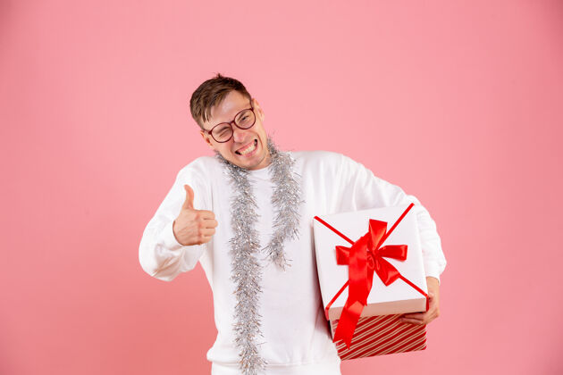 礼品盒粉红色墙上年轻人拿着圣诞礼物的正面图庆祝男性节日