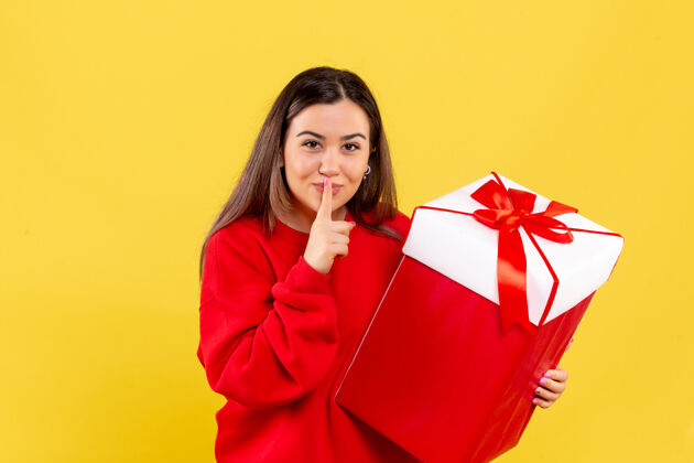 礼物盒黄色墙上手持圣诞礼物的年轻女子的正视图人们圣诞快乐微笑