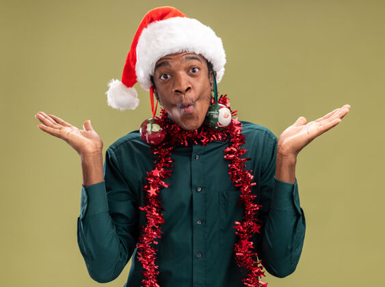 美国快乐的非洲裔美国人戴着圣诞帽 戴着花环 耳朵上戴着圣诞球 看着绿色背景下的摄像机 他玩得很开心耳朵非洲帽子