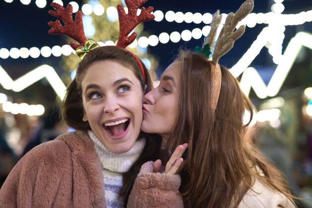 温暖感恩的女人在圣诞集市上亲吻举行城市给予