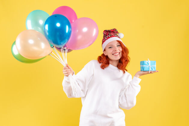 前面黄色墙上拿着小礼物和彩色气球的年轻女子的正视图生日年轻多彩