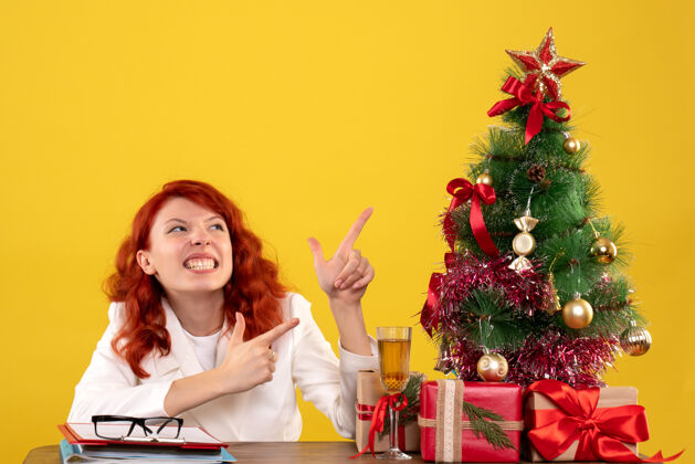 安排女工人坐在桌子后面 手里拿着圣诞礼物和黄色的圣诞树树成人坐着