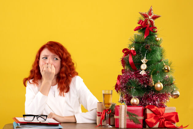 女女工人坐在桌子后面 手里拿着圣诞礼物和黄色的圣诞树工人桌子圣诞节