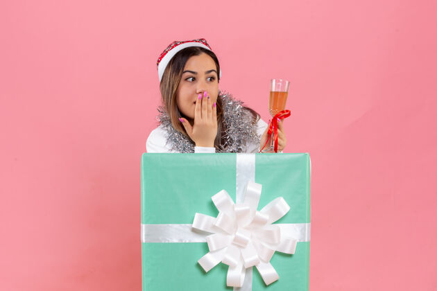 快乐前视图的年轻女子庆祝圣诞节与饮料上粉红色的墙壁圣诞节丝带礼物