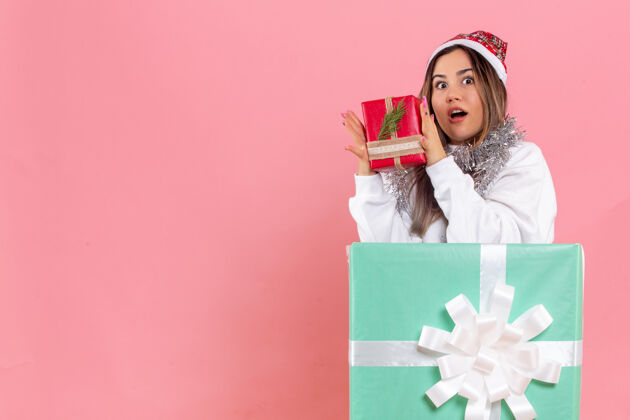 快乐一个年轻的女人拿着另一个礼物在粉红色的墙内的正面视图圣诞节漂亮人