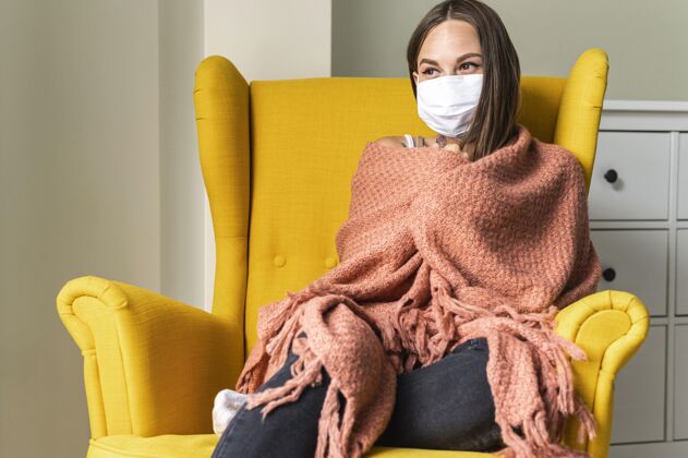 扶手椅大流行期间 一位妇女带着医用口罩坐在家里的扶手椅上隐居病毒女性