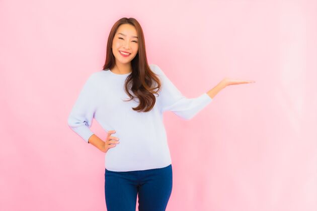 漂亮美丽的亚洲年轻女子在粉红色的隔离墙上微笑中国人手势韩语