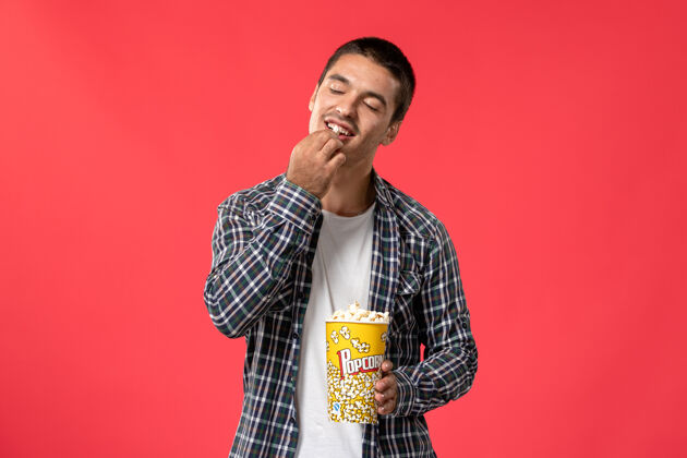 歌手正面图年轻男子拿着爆米花包在淡红墙电影院吃电影电影院年轻年轻男性
