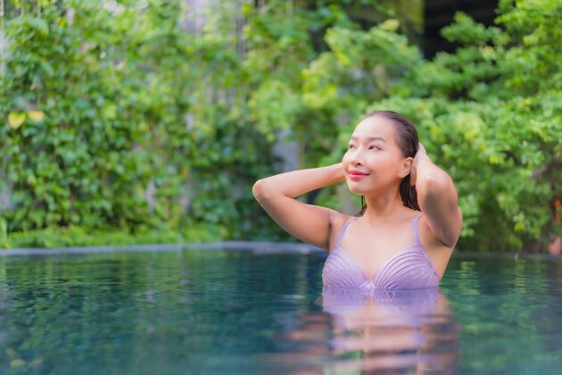 泳装肖像美丽的亚洲年轻女子放松微笑休闲在酒店度假村的室外游泳池周围年轻度假村天堂