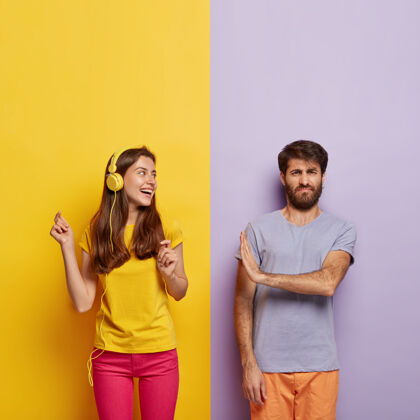 男性快乐无忧无虑的女人穿着休闲的黄色t恤 粉色裤子 戴着现代耳机听音乐声音科技在一起