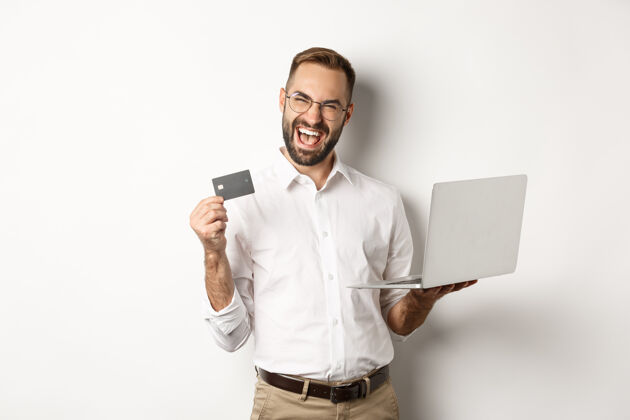 员工网上购物帅哥出示信用卡 用笔记本电脑在网上点菜 站着男人信用卡衬衫