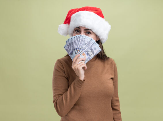 帽子年轻漂亮的女孩戴着圣诞帽 脸上镶着现金 背景是橄榄绿脸橄榄高兴